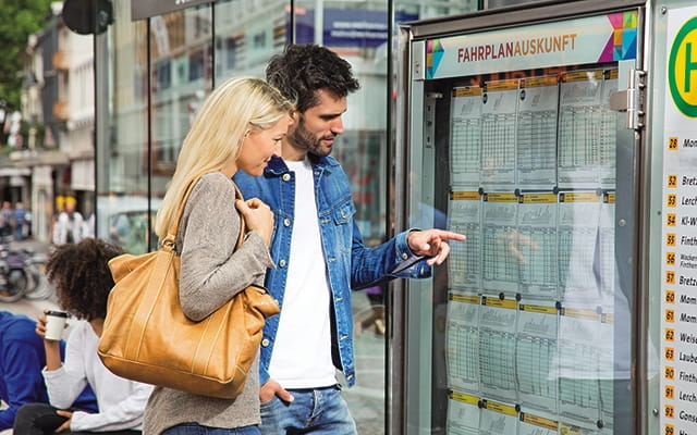 Junges Pärchen an einer Fahrplanauskunft der Mainzer Mobilität 2 Ein junges Pärchen steht an einer Haltestelle und schaut sich die Informationen an