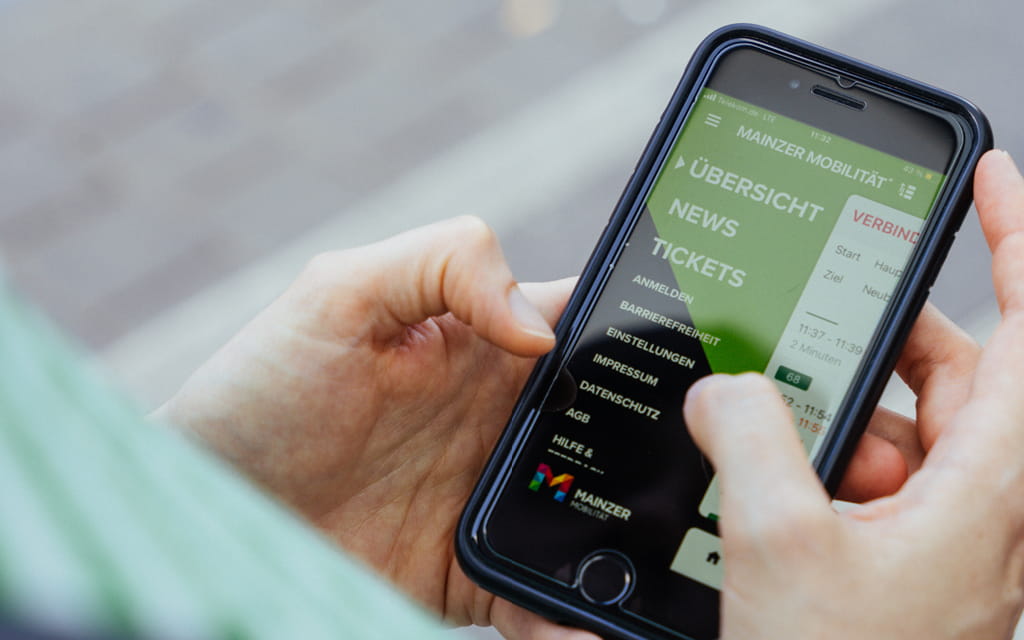 Foto, wie jemand ein Handy hält, auf dessen Bildschirm die Mainzer Mobilitaet-App angezeigt wird