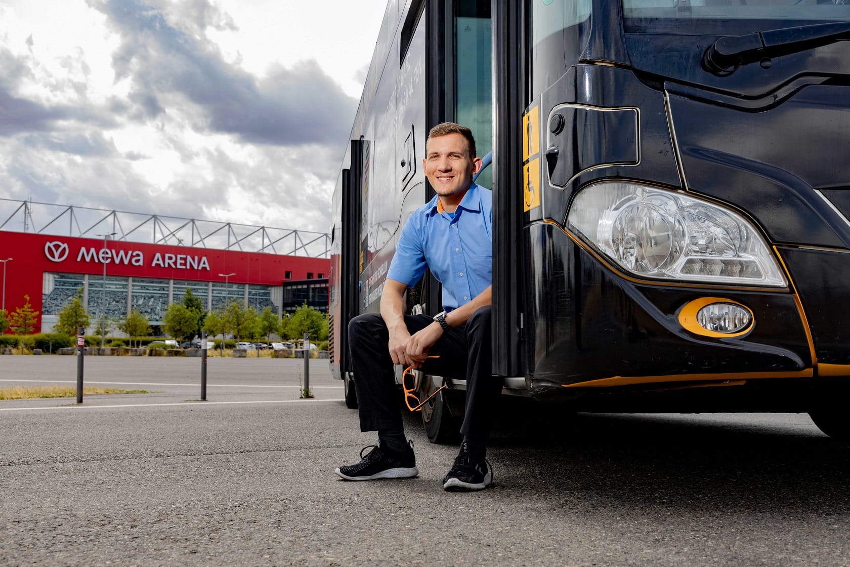 Busfahrer sitzt draußen in der Bustür mit Sonnenbrille in der Hand