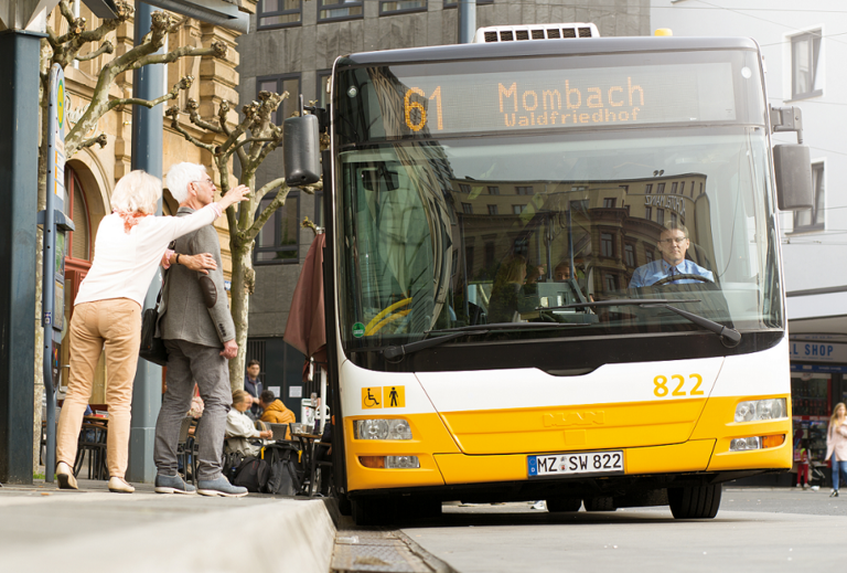 Ältere Menschen stehen an einer Haltestelle und winken dem Bus
