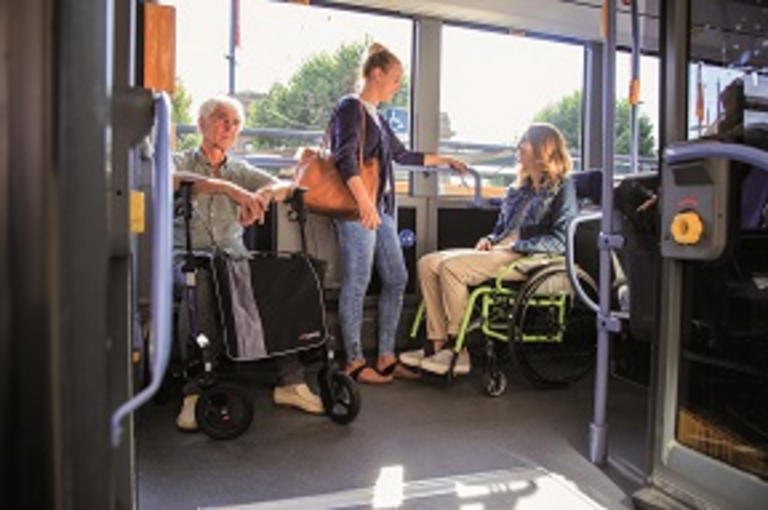 Ein Rollstuhlfahrerin  und ein Herr mit Rollator teilen sich die Mehrzweckfläche im Bus